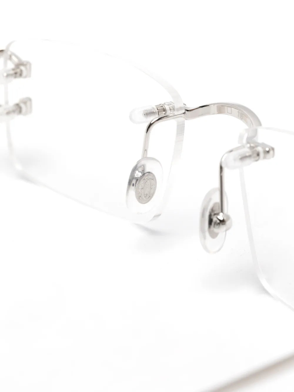 Close-up of a pair of rimless eyeglasses with clear lenses and silver metal hinge hardware on a white background.