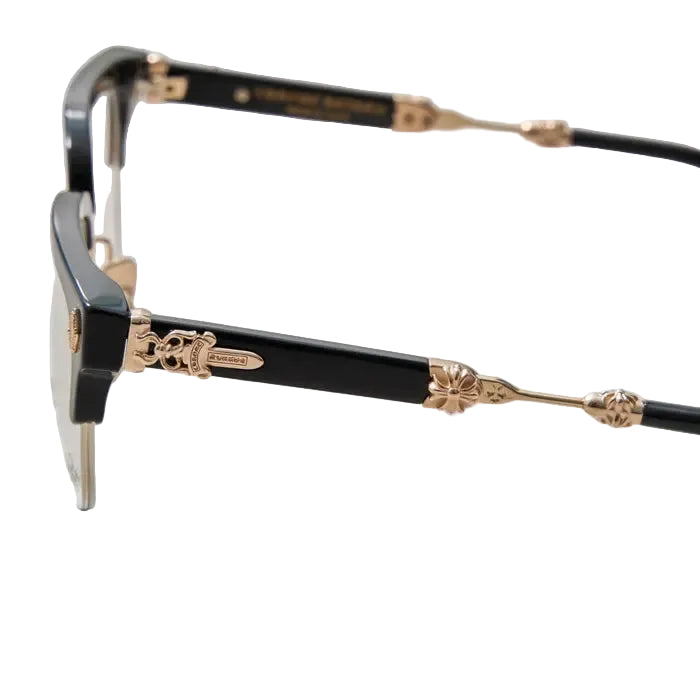Close-up of a pair of designer eyeglasses with a glossy black acetate frame and ornate gold-tone metal accents, resting on a light gray textured surface.