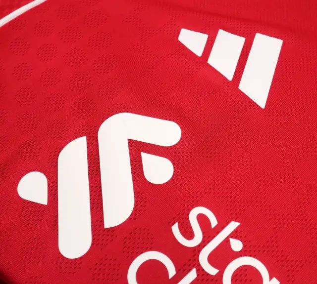 Close-up of a red athletic jersey with white printed sponsor logos and part of the Adidas three-stripe logo, showing textured mesh fabric.