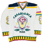 A vintage-style white knit sweater with colorful embroidered graphics, including 'LASABLANCA Tennis Club PARIS' and a central crest, laid flat on a beige textured surface.