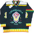 A vintage knit hockey-style sweater with 'LASABLANCA Tennis Club PARIS' text and a large central crest, laid flat on a beige faux-fur surface. The sweater is black with white shoulder panels, multicolor striped trim, and colorful graphic details.