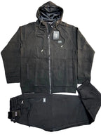 A black two-piece tracksuit laid flat on a gray textured background, featuring a zip-up hoodie with a hood and matching black jogger pants with drawstrings.