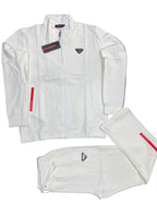A white Prada tracksuit set laid flat on a dark gray textured background, including a zip-up jacket with a small black triangle logo on the chest, matching sweatpants with a drawstring waist, and folded pants showing a red Prada label.