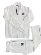 A white two-piece tracksuit laid flat on a dark gray textured background, featuring a zip-up jacket with a black 'MM' monogram on the left chest and matching sweatpants with a black logo on the right leg.