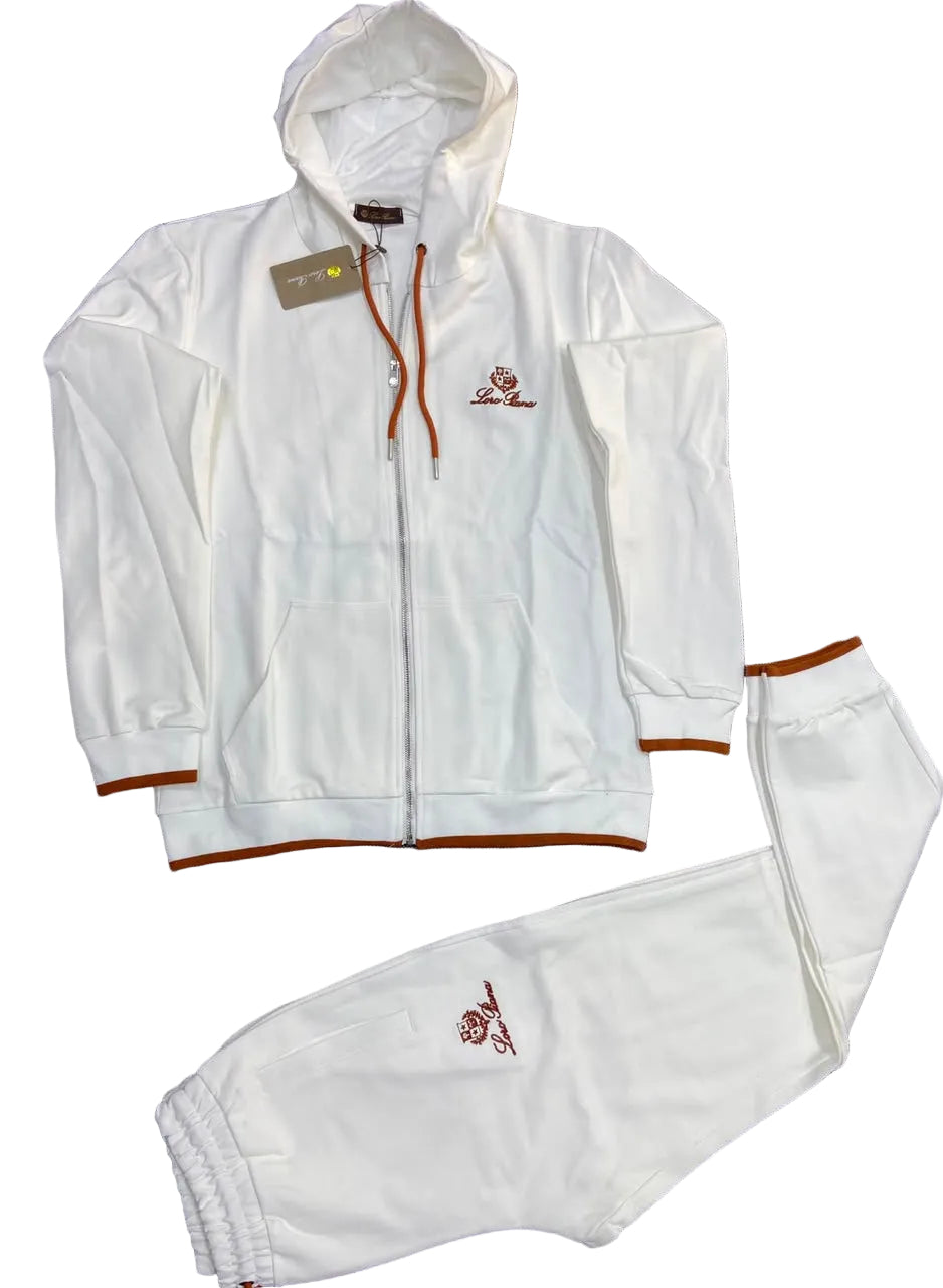 A white two-piece tracksuit set consisting of a zip-up hoodie and matching sweatpants, laid flat on a dark gray textured surface. The tracksuit features brown drawstrings, brown ribbed trim on the cuffs and hem, and a small embroidered logo on the left chest and left thigh.