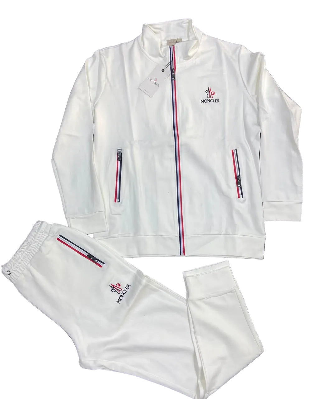 A white Moncler tracksuit set consisting of a zip-up jacket and matching sweatpants, laid flat on a dark gray textured background. The Moncler logo is embroidered on the left chest, and the iconic red, white, and blue stripe detail runs down the center zipper and the side pockets.