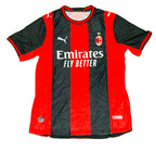 AC Milan home soccer jersey by Puma, featuring red and black vertical stripes with white sponsor and team logos, laid flat on green grass.