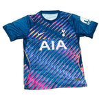 A blue Tottenham Hotspur soccer jersey with pink, orange, and yellow diagonal stripes, featuring the white AIA sponsor logo on the front, laid flat on green grass.