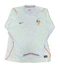 A white long-sleeve France national football team jersey by Nike, featuring orange piping, a blue collar, and the French crest on the chest, laid flat on green grass.
