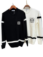 Two knit crewneck sweaters hanging on wooden hangers against a textured wall. The front sweater is black with white sleeve stripes, a white chest logo, and a white hem stripe.