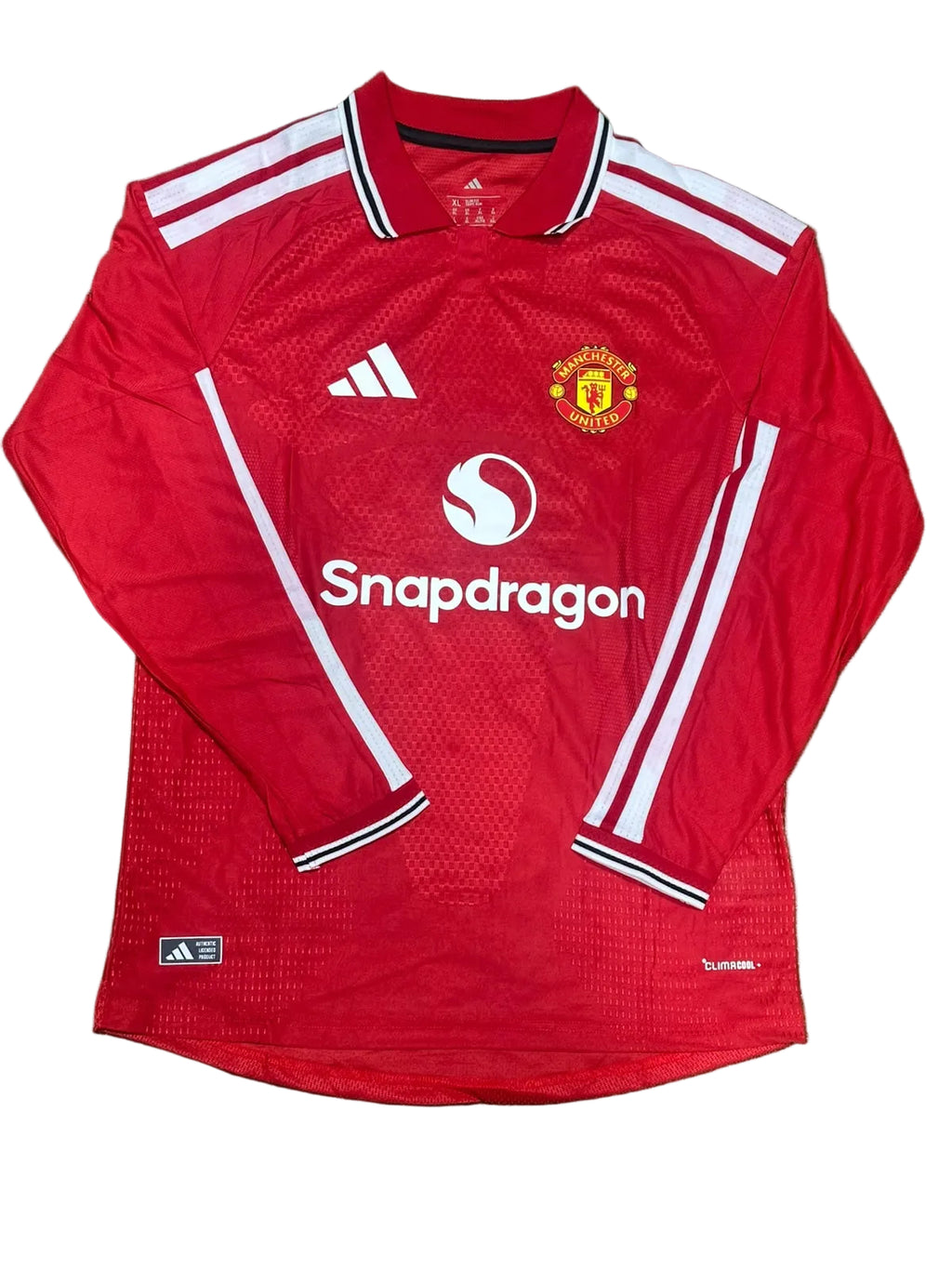 A red long-sleeve Manchester United soccer jersey with white stripes and the Snapdragon sponsor logo, laid flat on green artificial turf.