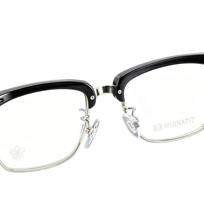 Close-up of a pair of eyeglasses with a glossy black upper frame, silver metal lower rims and hinges, clear nose pads, and clear lenses. The brand name 'MUINATIT' is printed on the lower right lens.