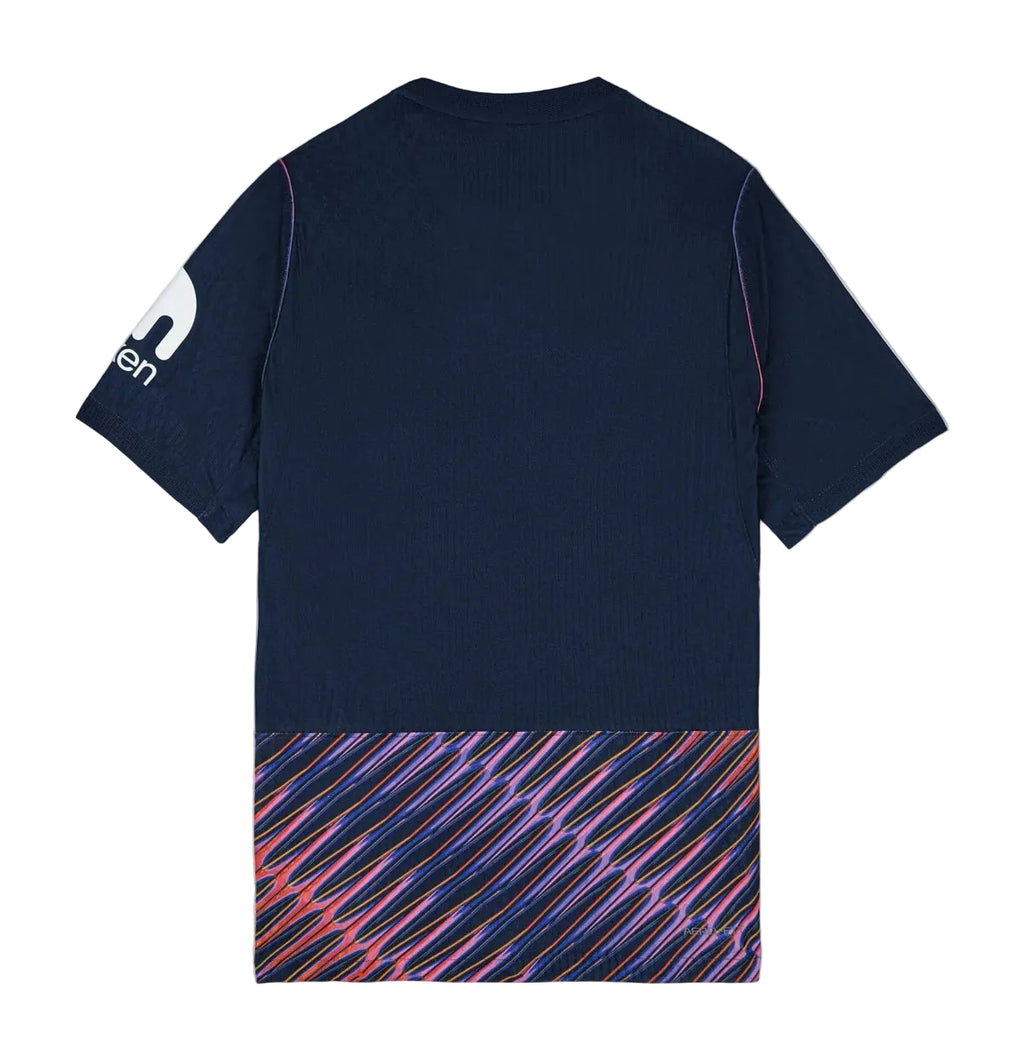 The back of a short-sleeve athletic t-shirt in dark navy blue, featuring a white logo on the left sleeve and a vibrant diagonal striped pattern in pink, purple, and blue along the bottom hem.